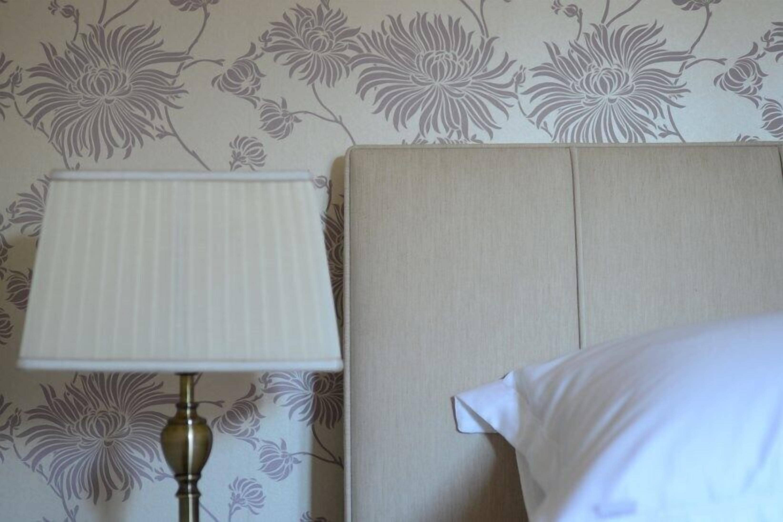 A room with a headboard, a lamp, and a floral wallpaper pattern.