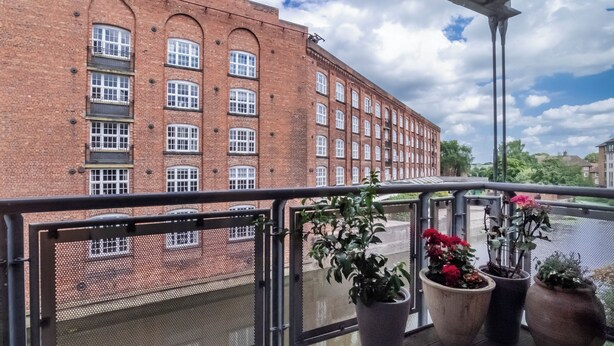 A balcony with potted plants and a view of a brick building with multiple windows. - 20 John Walker House (York)