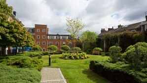 A courtyard with a paved walkway, neatly trimmed hedges, and a variety of flowering plants. - Skeldergate Apartment (York)