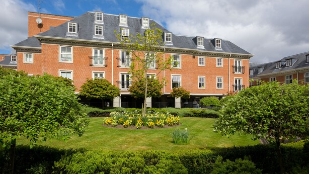 A large brick building with multiple windows and a well-maintained garden with various plants and flowers. - Skeldergate Apartment (York)