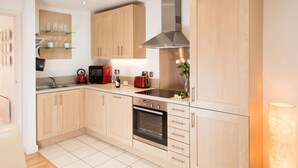 A modern kitchen with wooden cabinets, a stainless steel range hood, a built-in oven, and a countertop with glassware and a kettle. - Skeldergate Apartment (York)