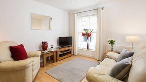 A modern living room with two sofas, a TV, a wooden side table, and a window with curtains. - Skeldergate Apartment (York)