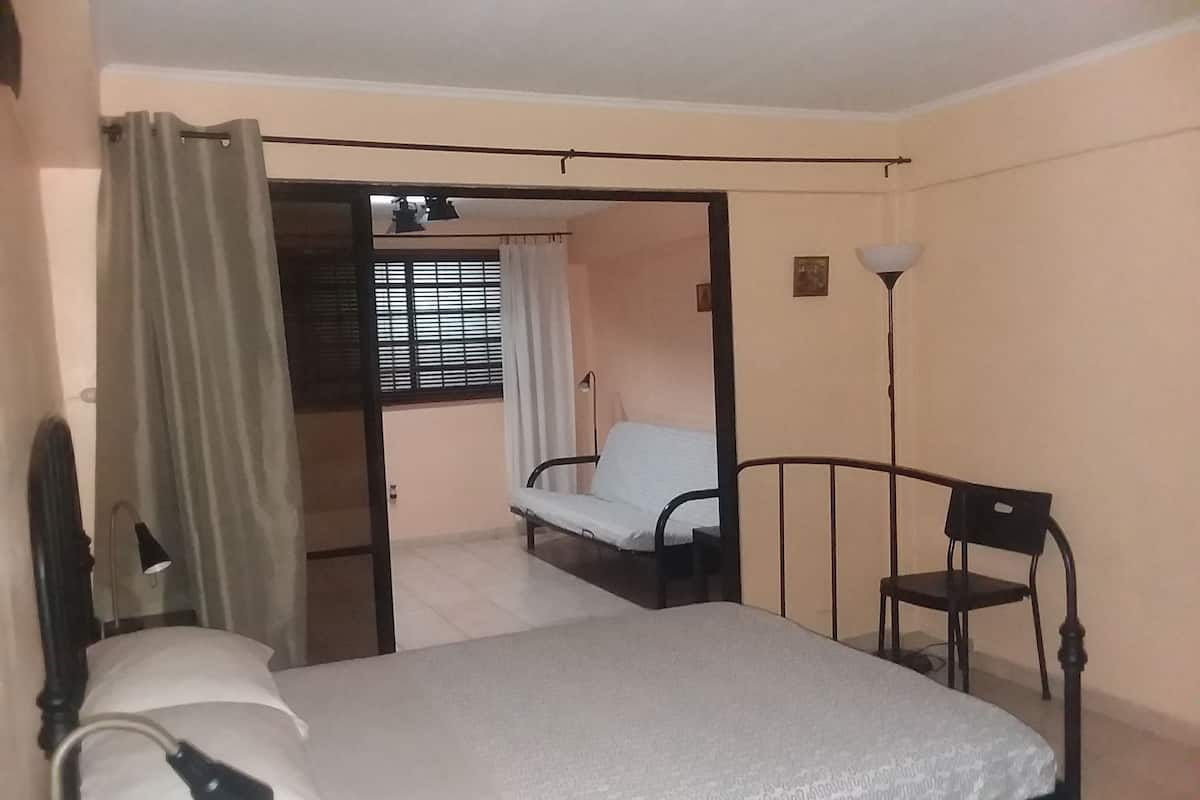 A bedroom with a bed, a chair, a desk, and a window with curtains.