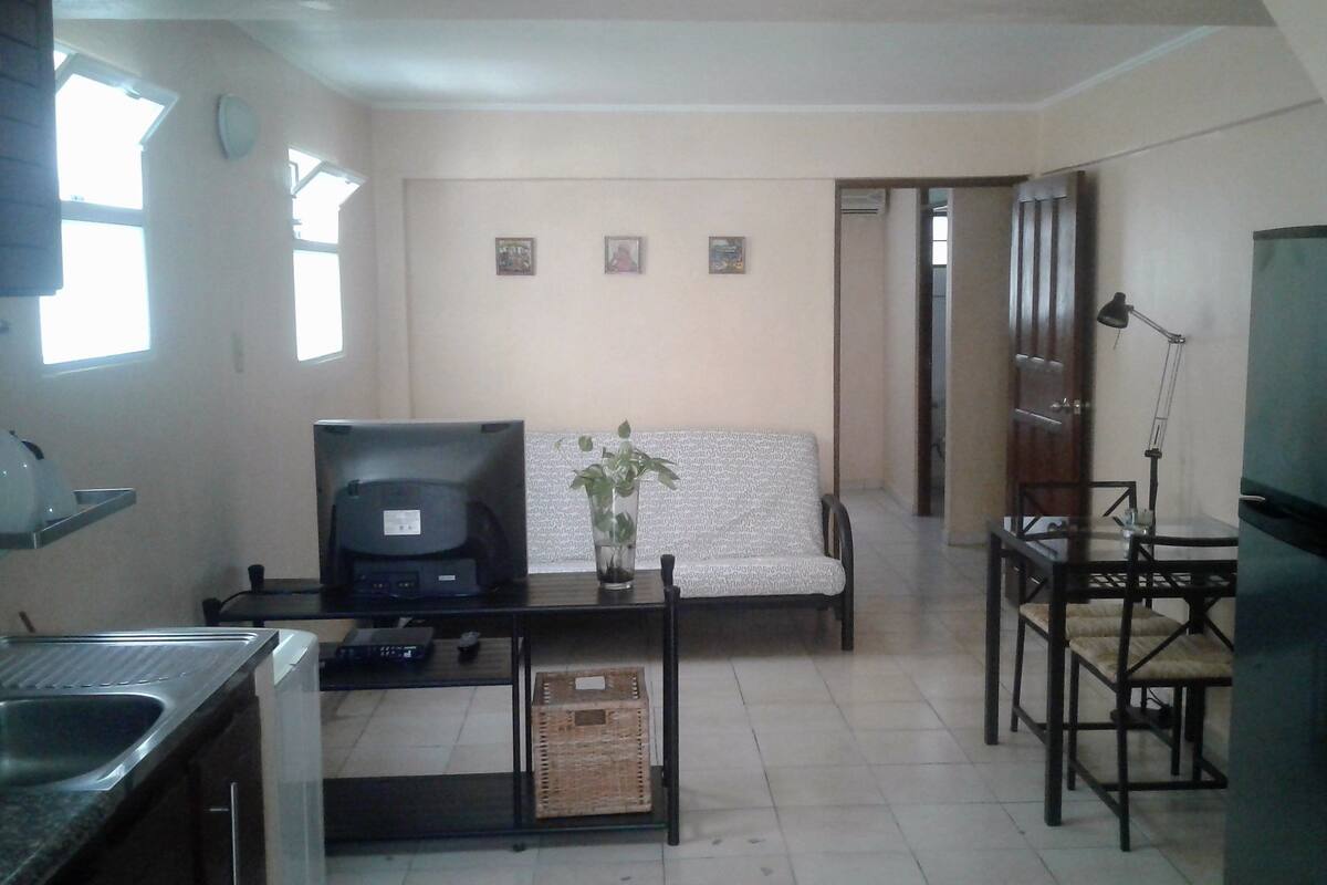 A compact living space with a kitchenette, a sofa, a dining table, and a refrigerator.