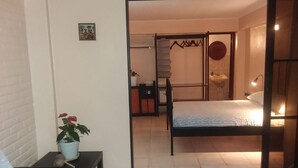 Ein Schlafzimmer mit einem Bett, einem kleinen Tisch mit Pflanze, einer Wanduhr und einer Schiebetür zu einem Badezimmer mit Waschbecken und Spiegel.