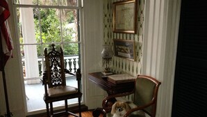 Una habitación con una silla de madera, un escritorio con una lámpara y un cuadro en la pared.