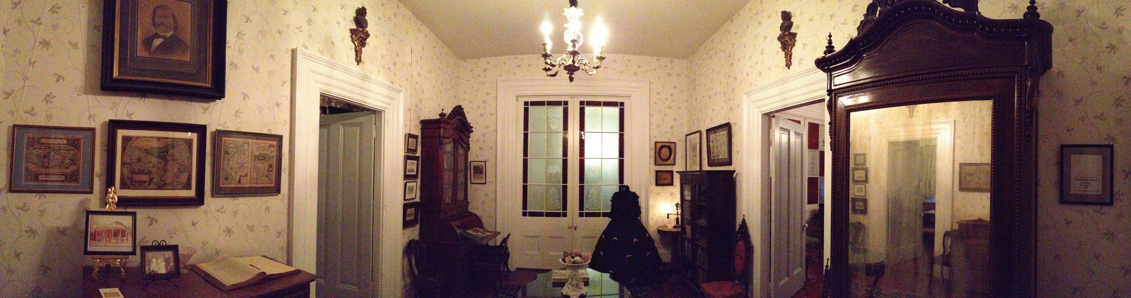 A dimly lit hallway with framed pictures on the walls, a chandelier, and a large mirror.
