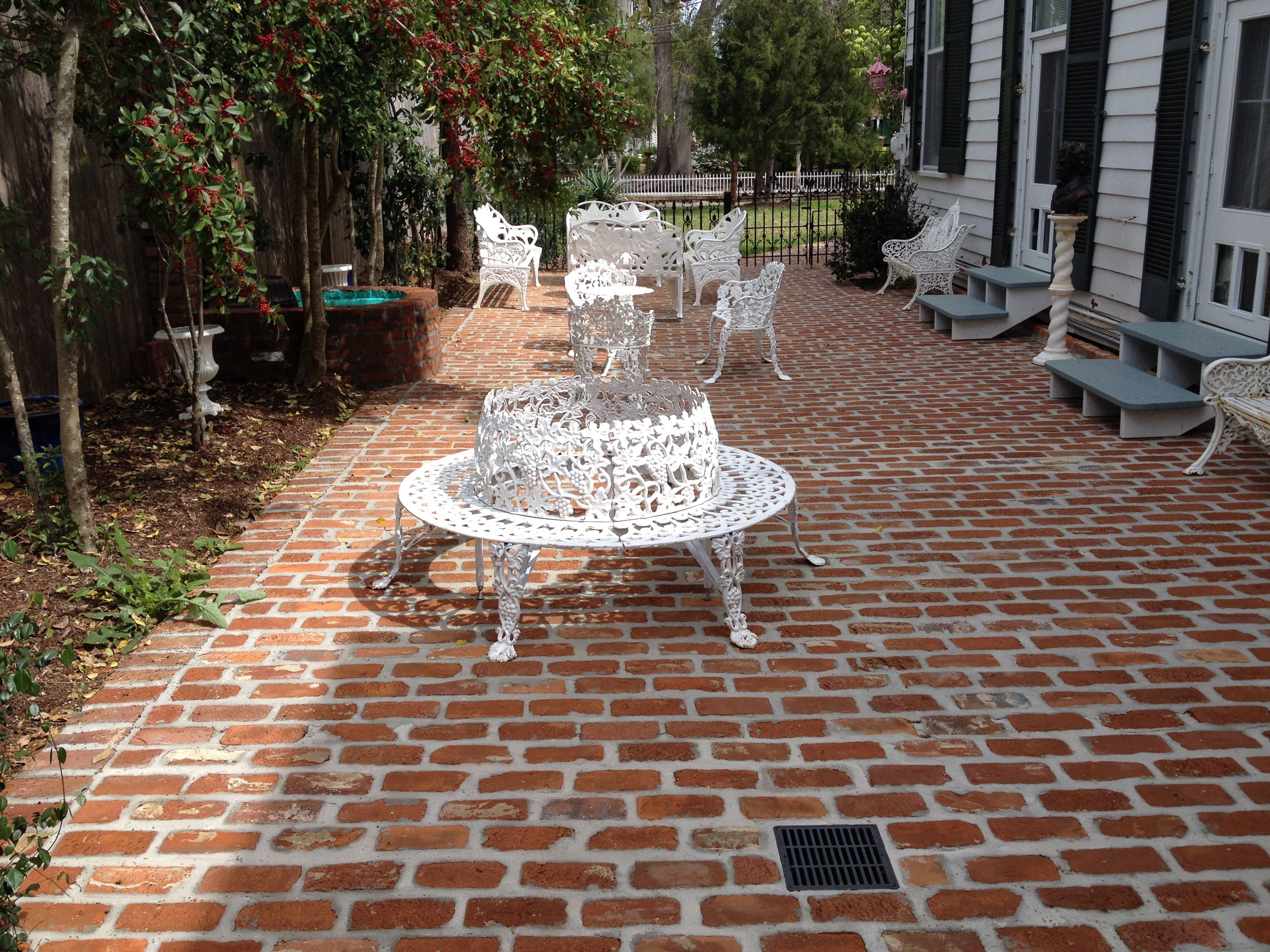 A patio with a brick floor, white metal chairs, and a central table.