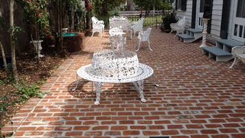 A patio with a brick floor, white metal chairs, and a central table.
