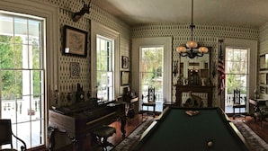 Una habitación con mesa de billar, chimenea y ventanas amplias.