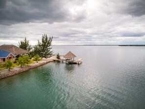 Un resort tranquilo frente a la playa, con cabañas de techo de paja, palmeras y un mar apacible bajo un cielo nublado.