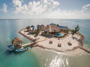 Un resort tropical con bungalows de techo de paja, una piscina y un muelle con barcos.