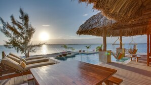 Une terrasse en bois avec des chaises longues et une piscine, offrant une vue sur l’océan.