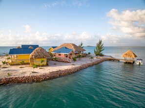 Un resort costero con cabañas de techo de paja, una playa arenosa y una vista despejada del mar.