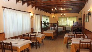 A dining area with multiple tables and chairs, wooden beams on the ceiling, and a wine rack in the background. - Catalan Hotel (Puerto Real)