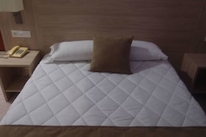 A hotel room with a bed, a bedside telephone, and a nightstand. - Catalan Hotel (Puerto Real)