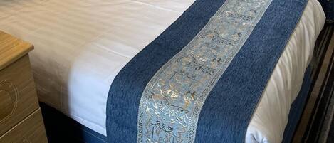 A hotel room with two beds, a nightstand, a lamp, and a window with curtains.