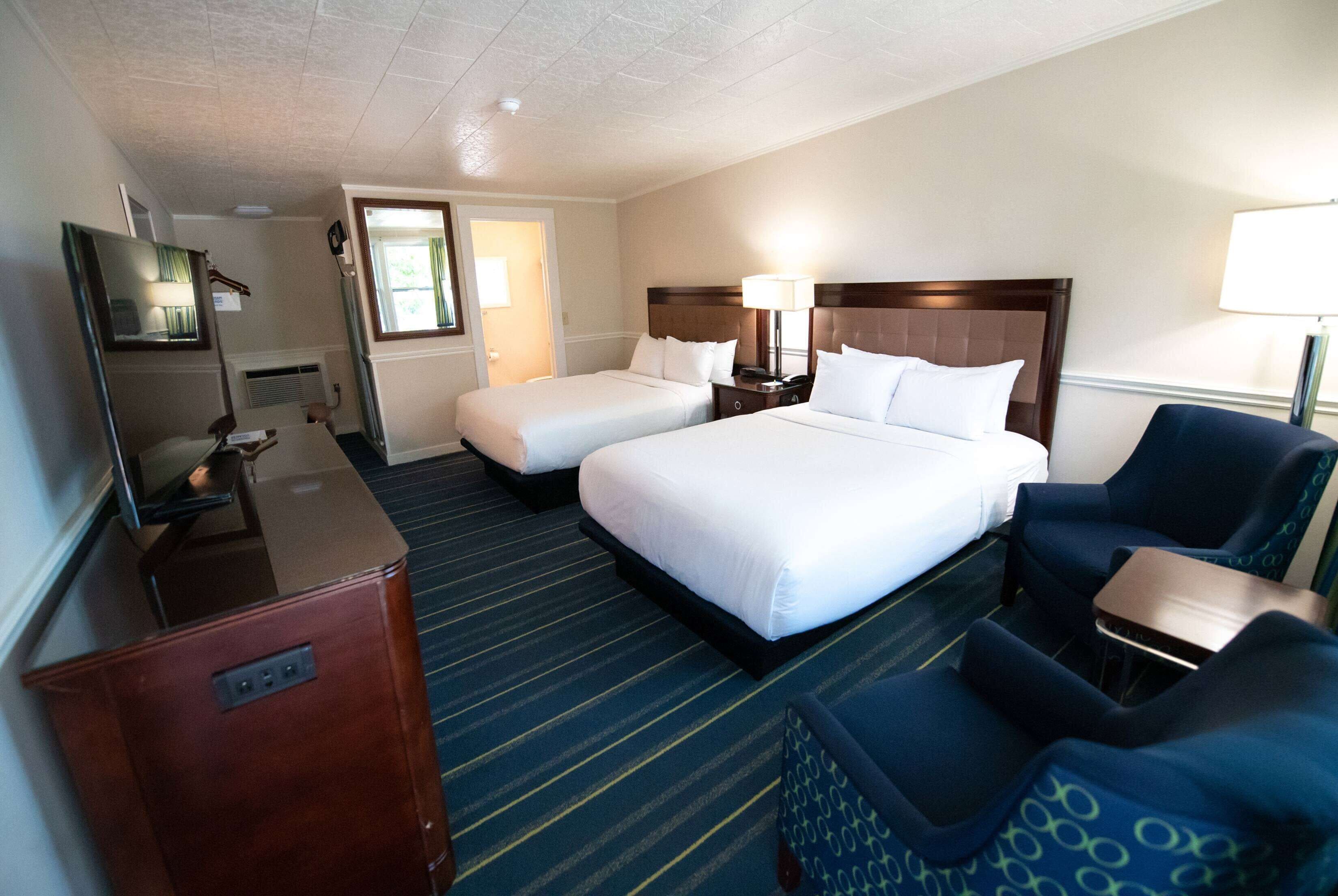 A hotel room with two beds, a desk, a chair, a TV, and a door leading to another room.