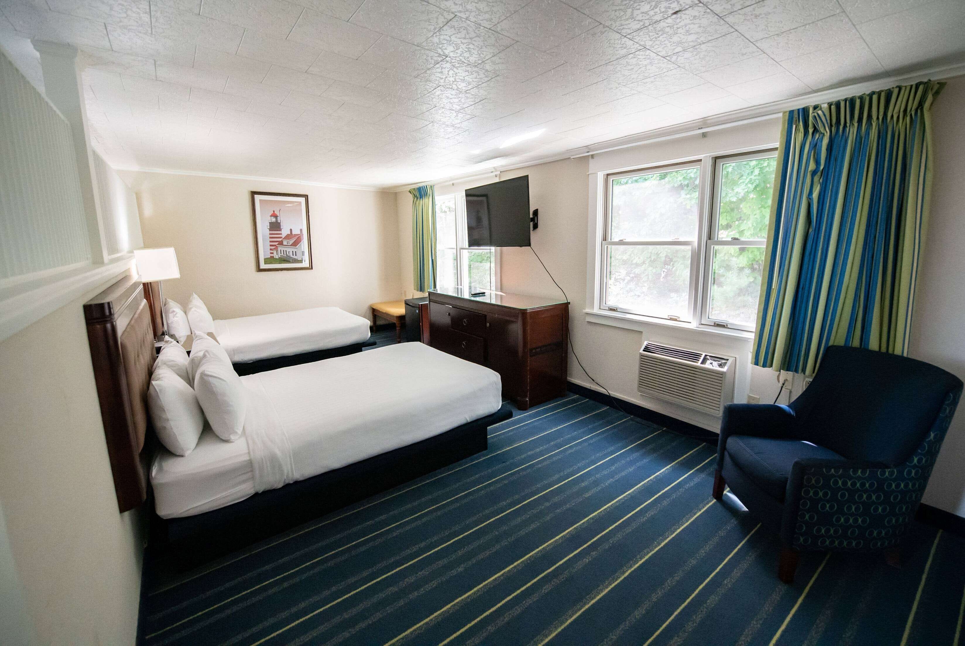 Ein Hotelzimmer mit Bett, Schreibtisch, Stuhl, Fernseher und einem Fenster mit Vorhängen.