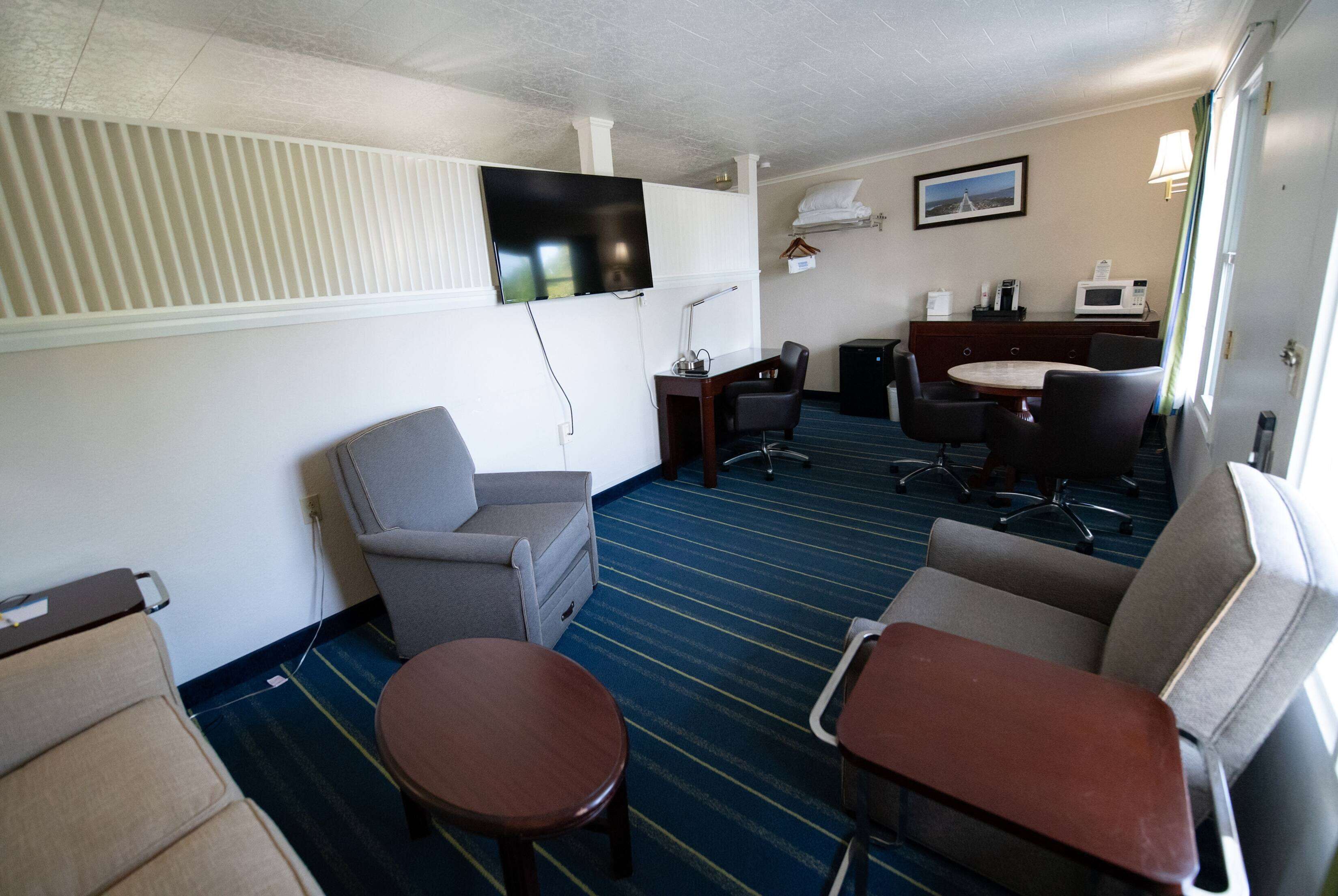 A hotel room with a TV, a desk with a computer, a chair, a sofa, and a small table.