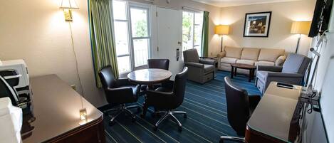 A hotel room with a dining table, chairs, a sofa, a TV, and a window with curtains.