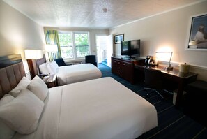 A hotel room with two beds, a desk, a television, and a window with a view of the outdoors.
