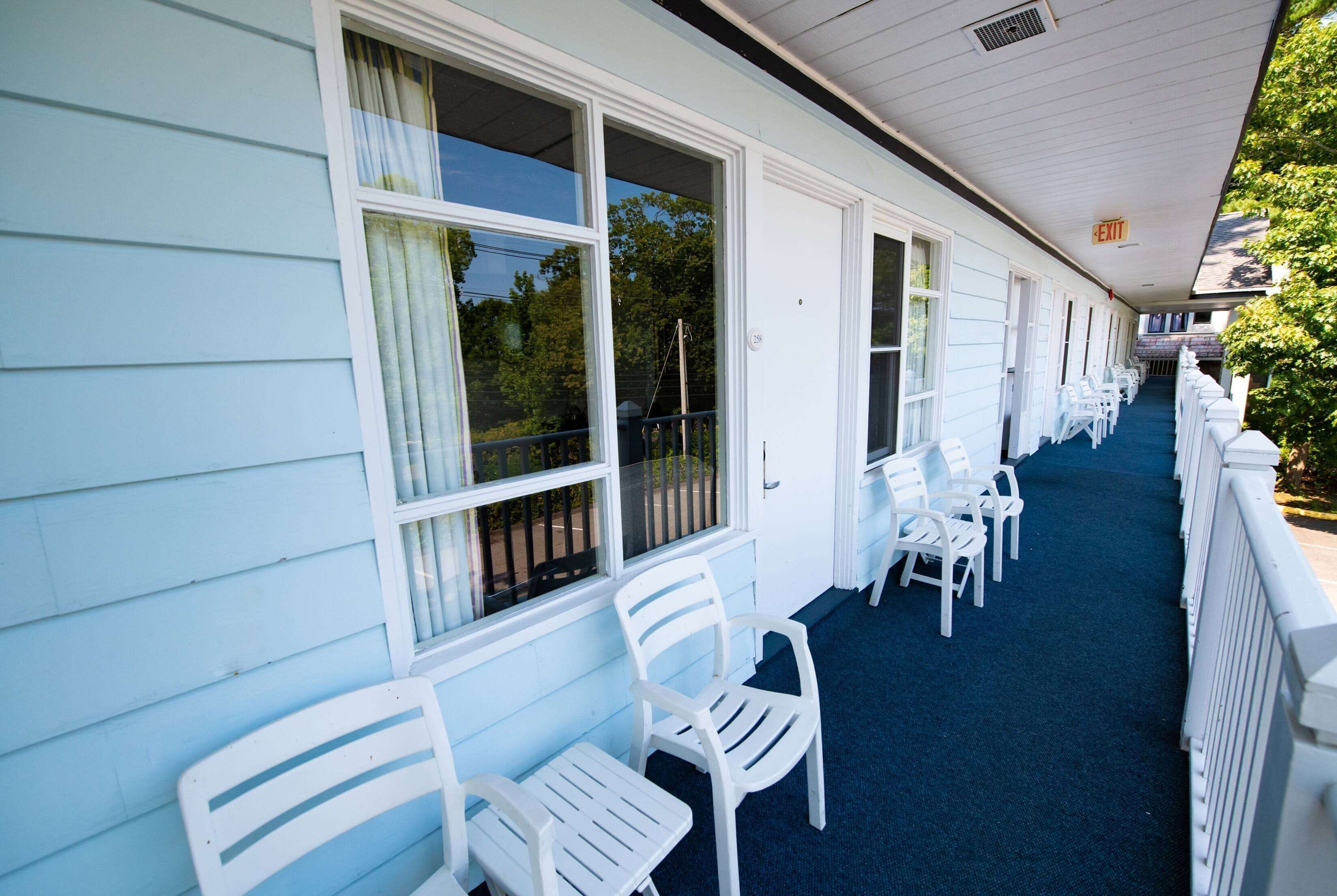A covered corridor with white chairs and tables, large windows, and a blue carpet.