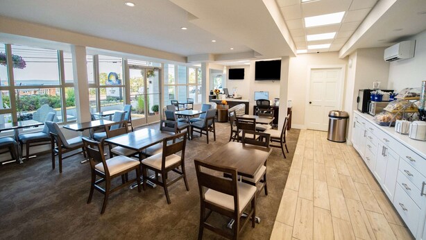 A hotel lobby with multiple dining tables and chairs, a kitchen area with a coffee machine, and a large window offering a view of the outside. - Days Inn Bar Harbor (Bar Harbor)