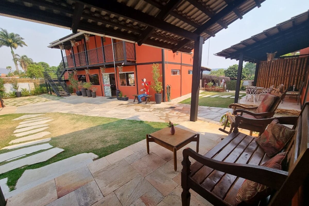 A covered patio area with stone flooring, wooden furniture, and a red building in the background.