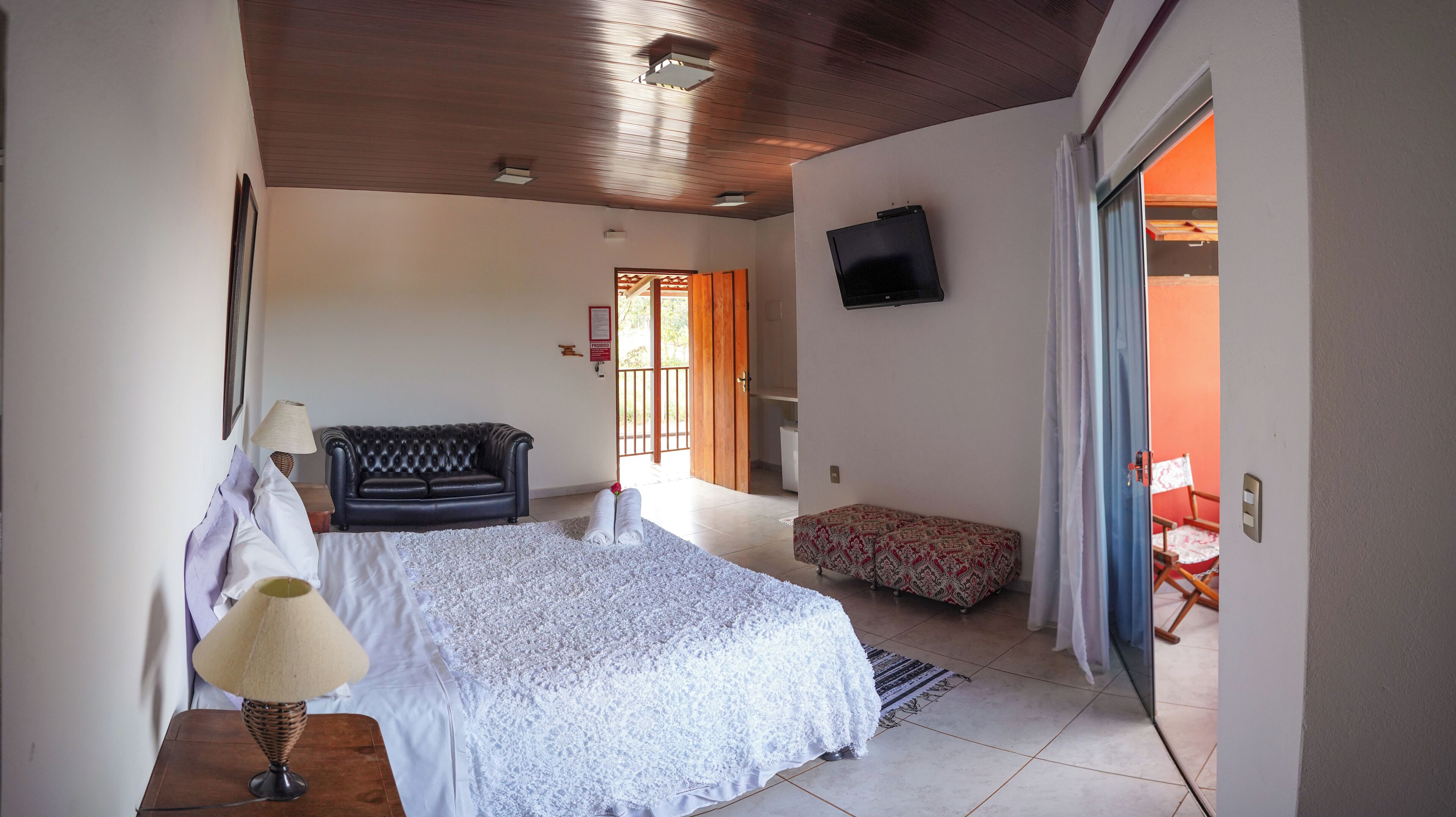 Quarto com uma cama grande, um sofá pequeno, uma TV na parede e uma porta de correr para área externa.