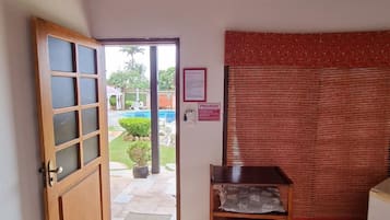 A room with a wooden door, a ceiling fan, a red curtain, and a small table with a cushion.