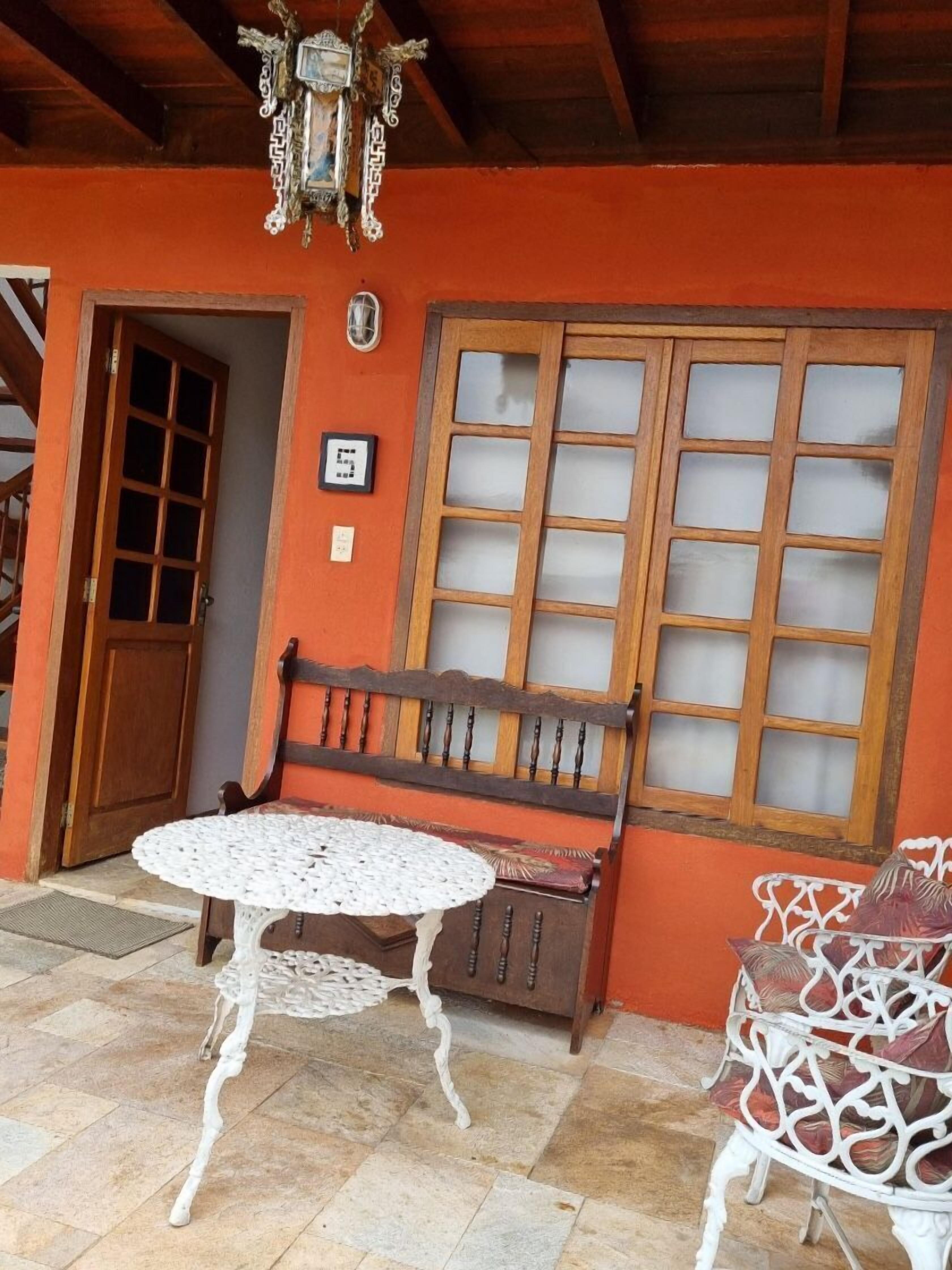 Quarto com um banco de madeira, uma mesa branca e uma cadeira estampada.
