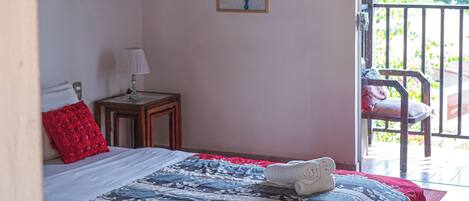 A bedroom with a bed, a nightstand, a lamp, and a window with a view of greenery.