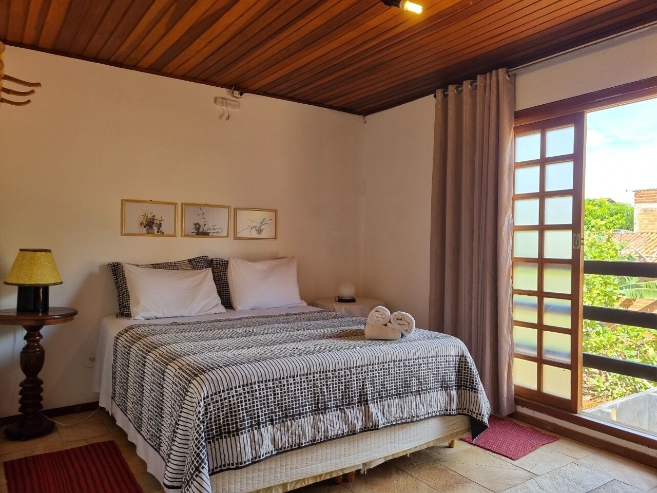 A bedroom with a bed, a nightstand, a lamp, and a window with curtains.
