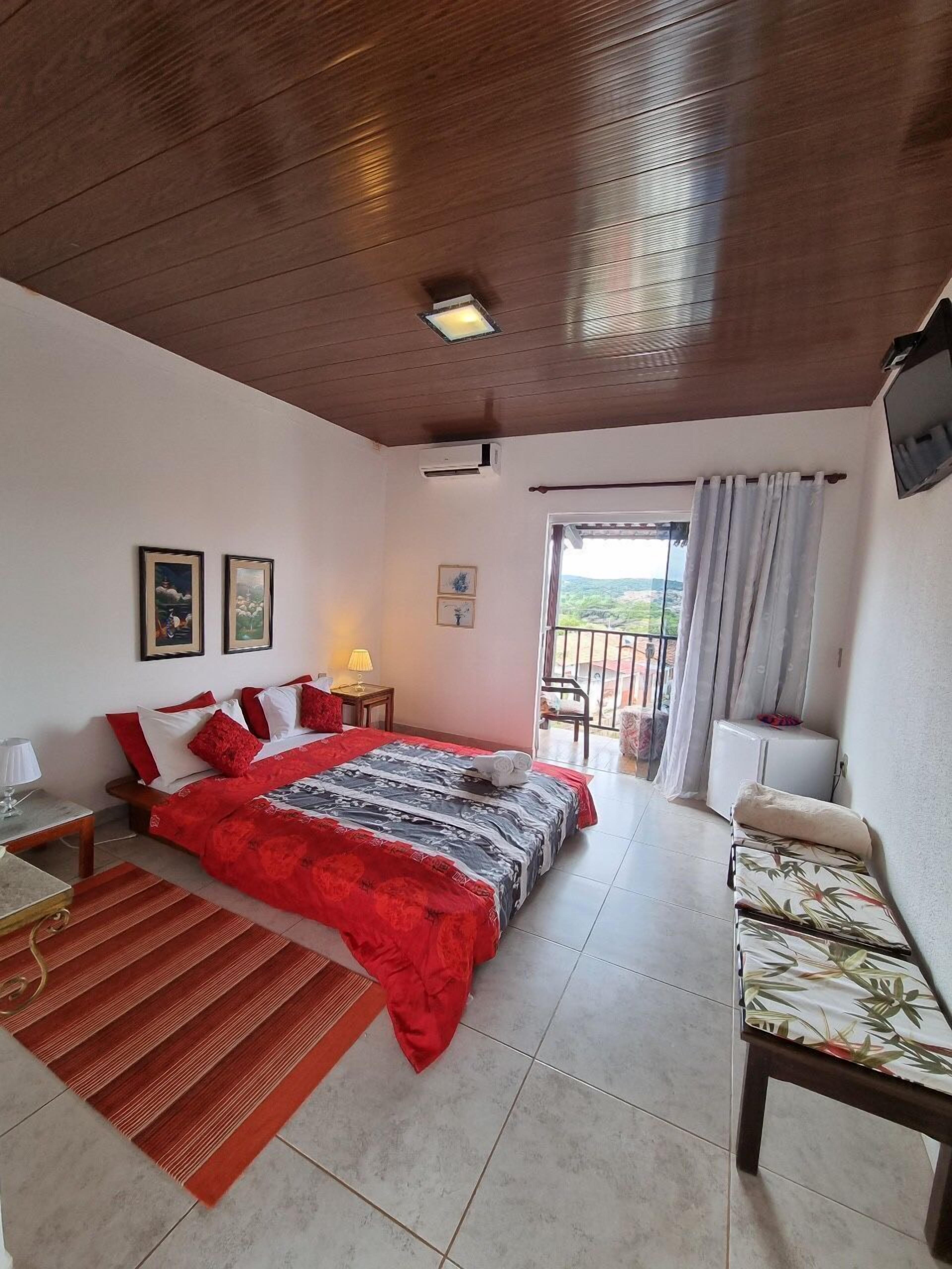 Une chambre à coucher comprenant un lit, une chaise, une petite table, une fenêtre avec des rideaux et une vue sur l’extérieur.