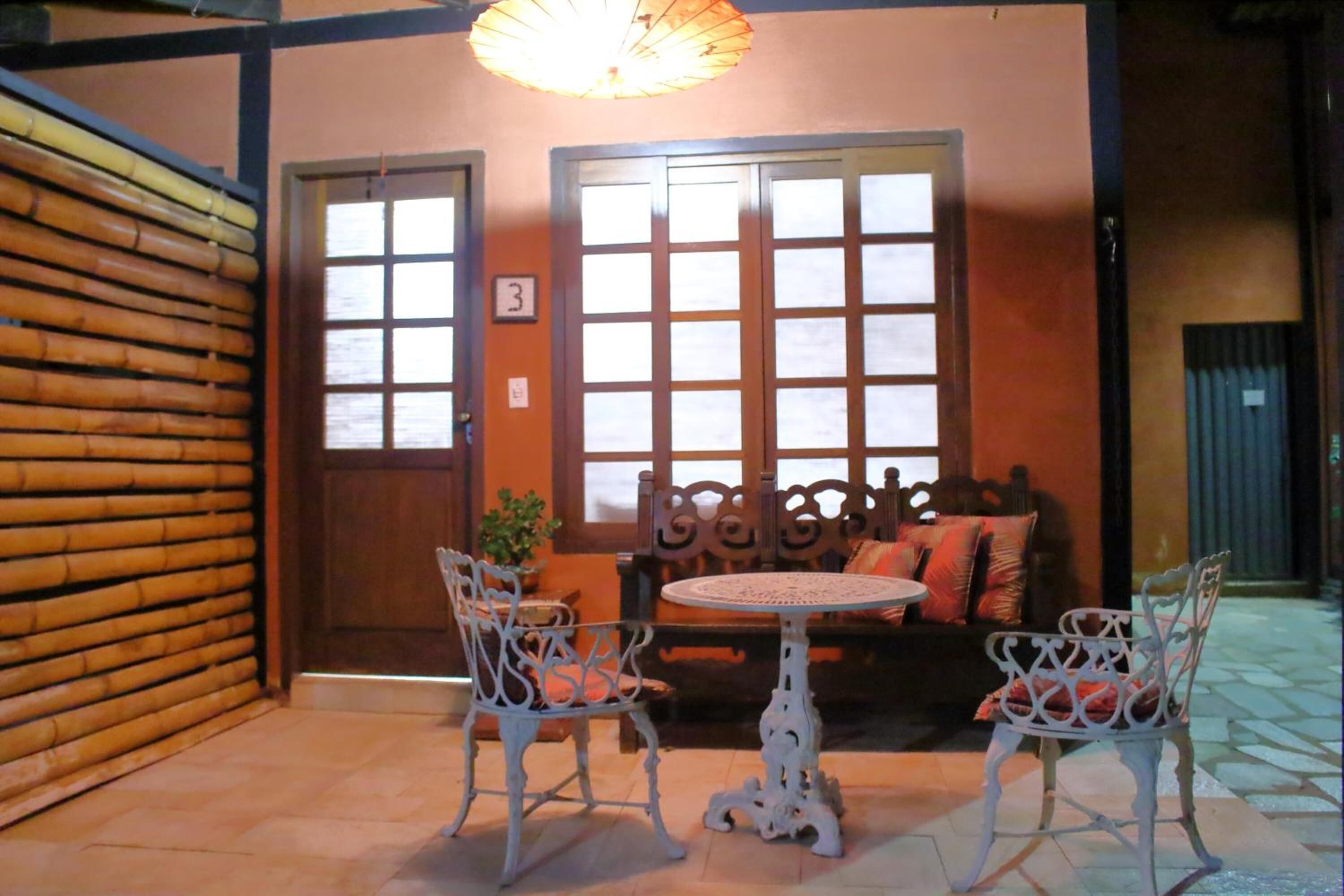 A cozy indoor seating area with a wooden door, a number '3' sign, and two white chairs with red cushions around a small round table.
