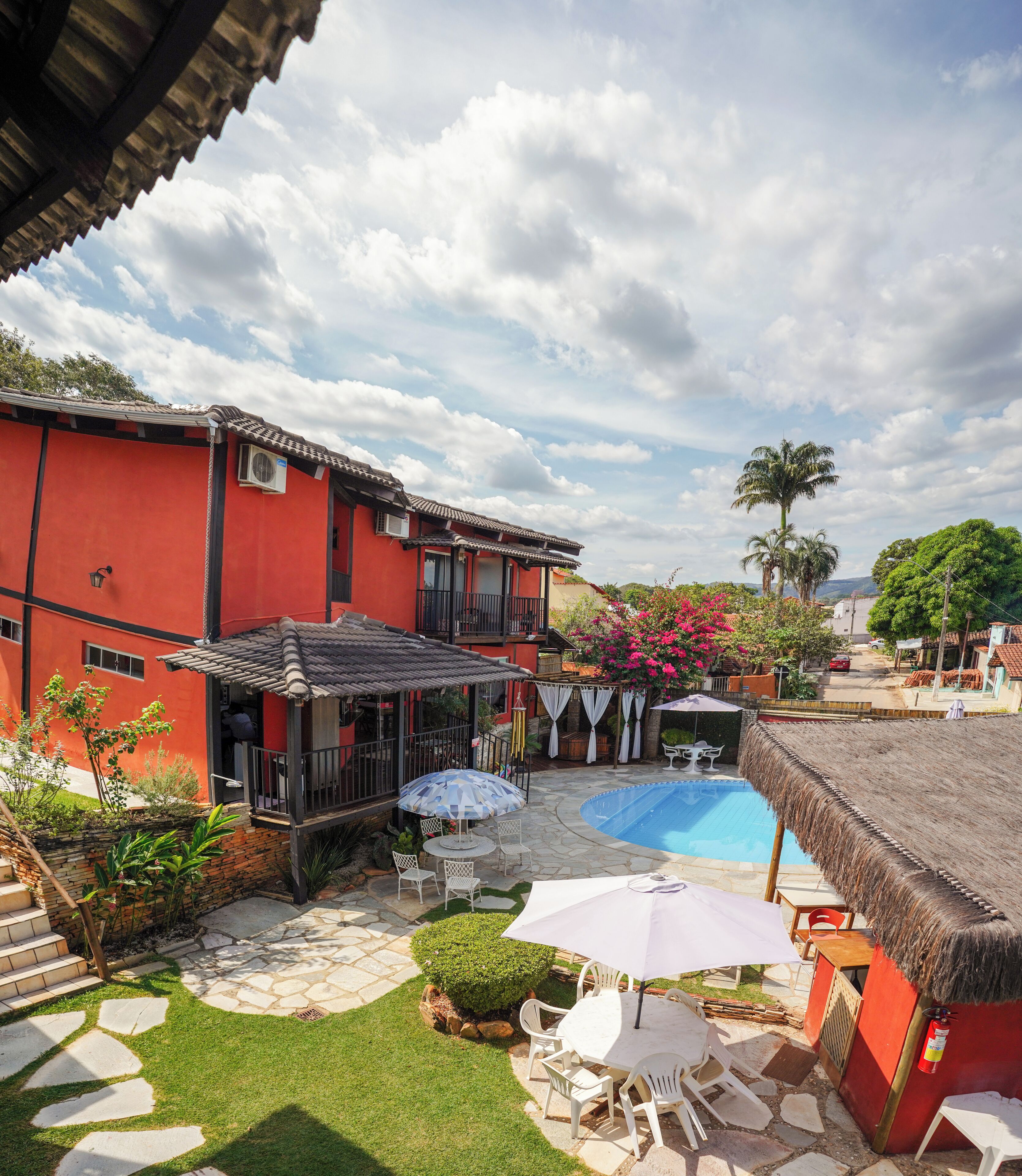 Un edificio rojo con piscina, asientos al aire libre y una estructura con techo de paja.
