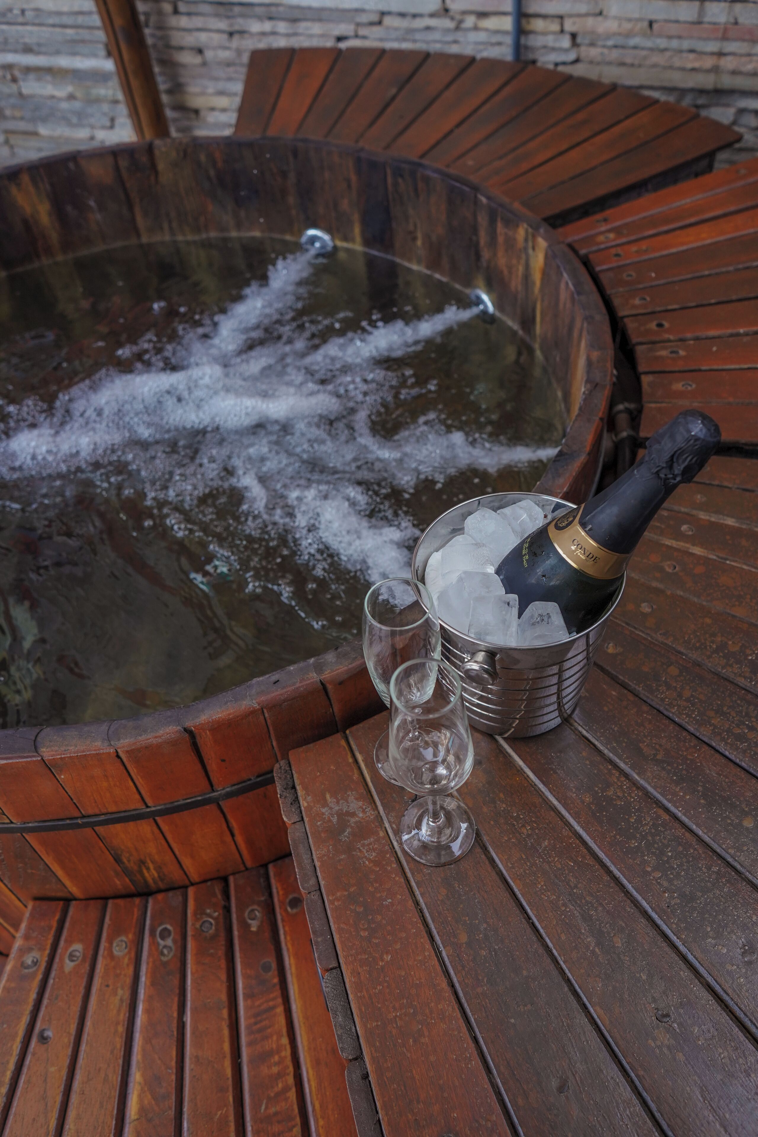 A hot tub with a bottle of champagne and two glasses on a wooden table.
