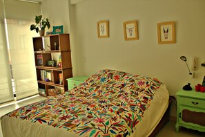 A bedroom with a bed, a bookshelf, and a desk with a lamp.