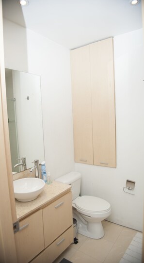 A bathroom with a white sink, mirror, and toilet. There is a wooden cabinet above the sink and a wooden door in the background.