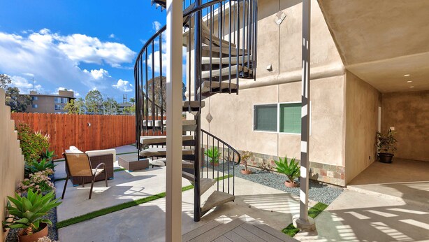 Un patio moderno al aire libre con una escalera espiral, mobiliario exterior y plantas en macetas.