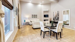 Amplia sala de estar con una mesa de comedor, sofás blancos y un televisor montado en la pared.
