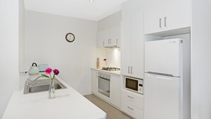 A modern kitchen with white cabinetry, a stainless steel sink, a microwave, an oven, and a refrigerator. - Astra Apartments Glen Waverley at VIQI (Glen Waverley)