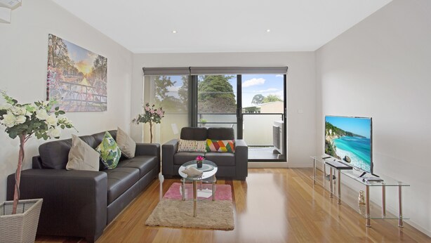 A modern living room with a sofa, coffee table, and a TV displaying a scenic view. - Astra Apartments Glen Waverley at VIQI (Glen Waverley)