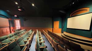 A theater with rows of green and brown seats, a large screen, and a stage area. - Orlando Oasis (Kissimmee)