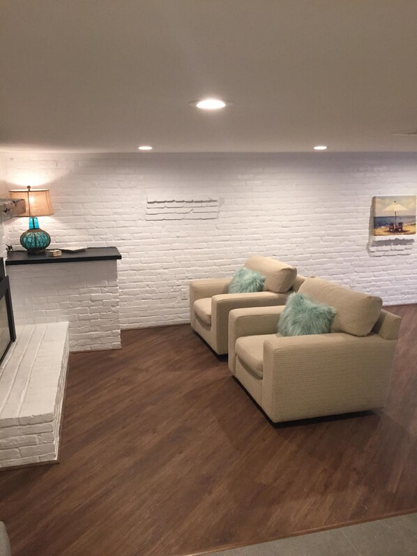 A living room with a white brick wall, two beige sofas with blue cushions, a wooden coffee table, a lamp, and a framed picture on the wall.