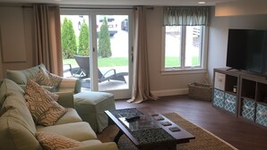 A living room with a sofa, a coffee table, a TV, and a sliding glass door leading to a patio. - Beautiful Provincetown 2 bedroom  centrally located (Provincetown)