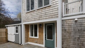 A two-story house with a front door, a small attached garage, and a wooden deck. - Beautiful Provincetown 2 bedroom  centrally located (Provincetown)