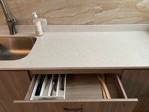 A kitchen with a stainless steel sink, a soap dispenser, and a drawer with utensils. - Segovia Studio Units (Carolina)