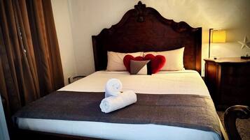 A neatly made bed with a rolled towel, a headboard, and a bedside lamp.